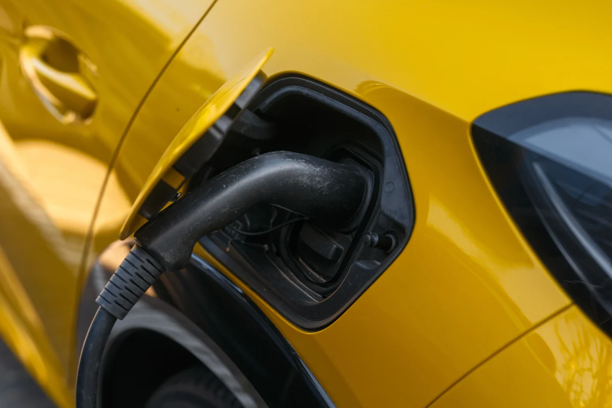 Sokakta park etmiş sarı elektrikli otomobilin şarj girişine bağlı kablo