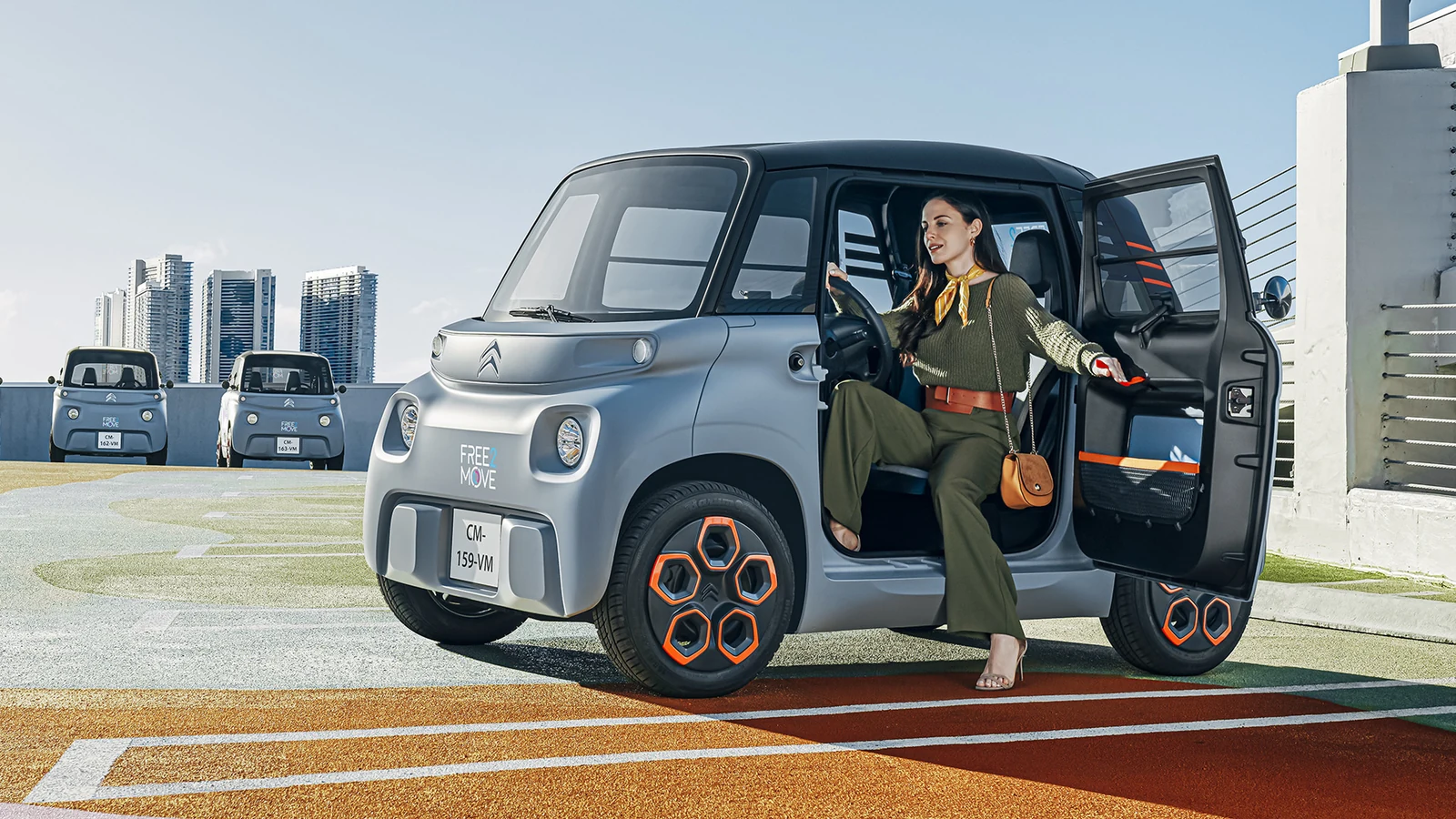 Gri Citroën Ami, şehir terasında açık sürücü kapısı ve kompakt gövde oranlarıyla